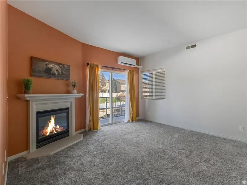 Fireplace with a classic mantel, gray carpeting, sliding glass doors to outdoor space, horizontal window blinds, and a wall-mounted mini-split unit