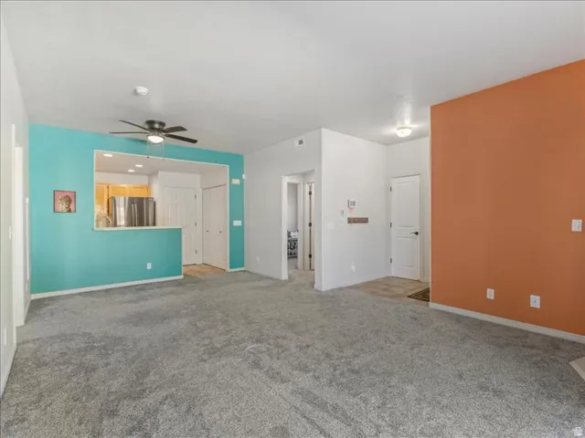 Gray carpeted flooring, a kitchen pass-through with a breakfast bar, a ceiling fan, and accent walls
