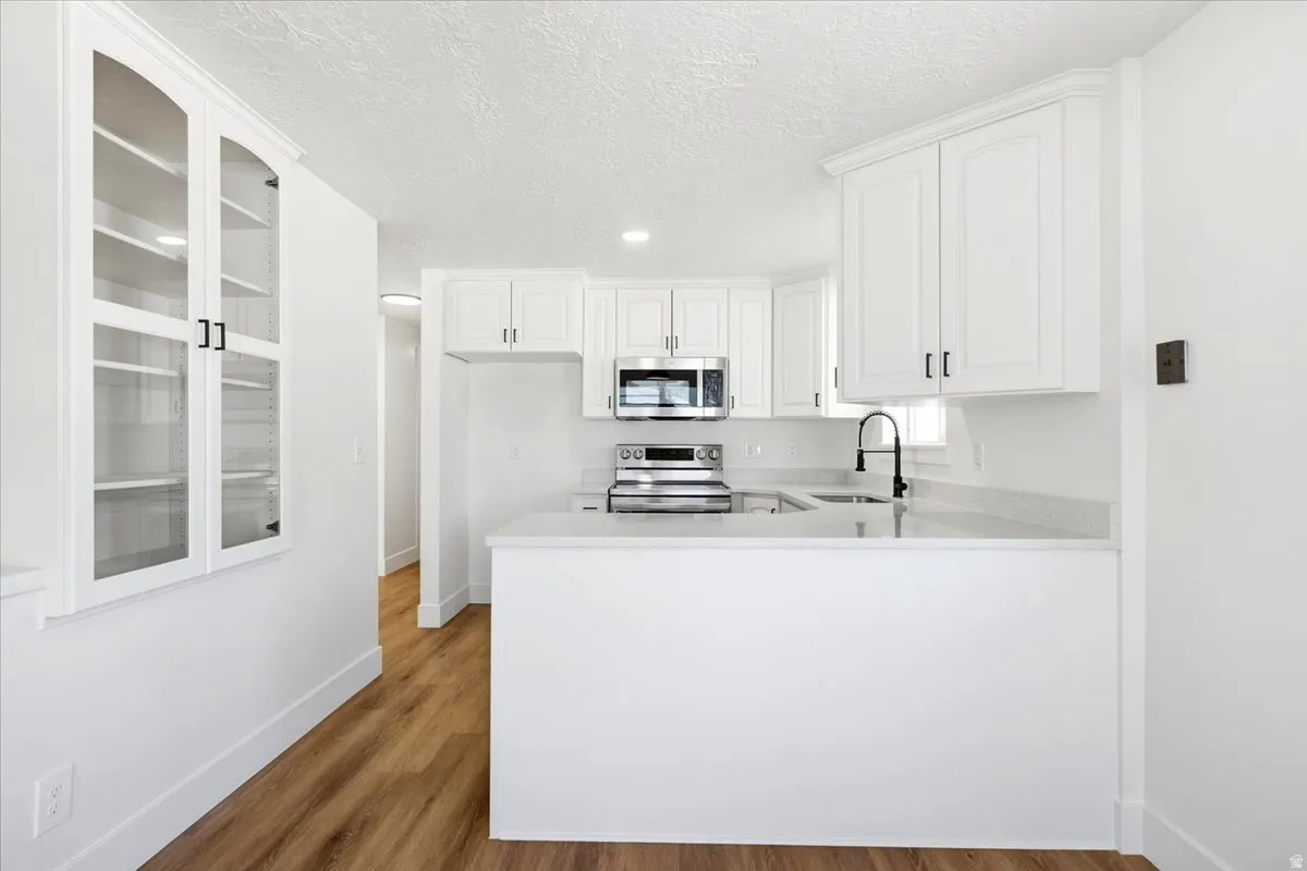 Kitchen featuring white cabinetry, stainless steel appliances, a matte black faucet, light countertops, and wood-finish flooring