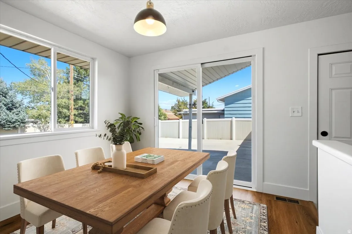 Bright interior with wood-finish flooring, a large window, a sliding glass door, a contemporary pendant light fixture, and a paneled interior door
