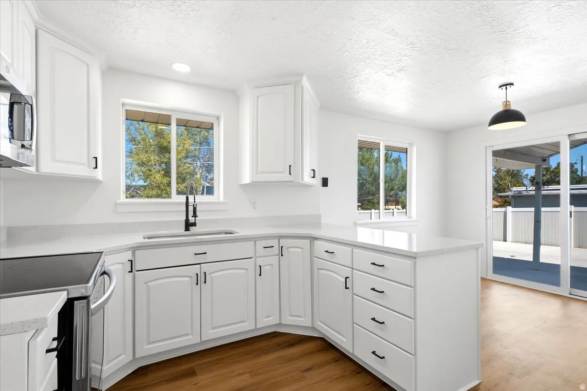 White cabinetry with dark hardware, stainless steel appliances, light-toned countertops, wood-finish flooring, and sliding glass doors