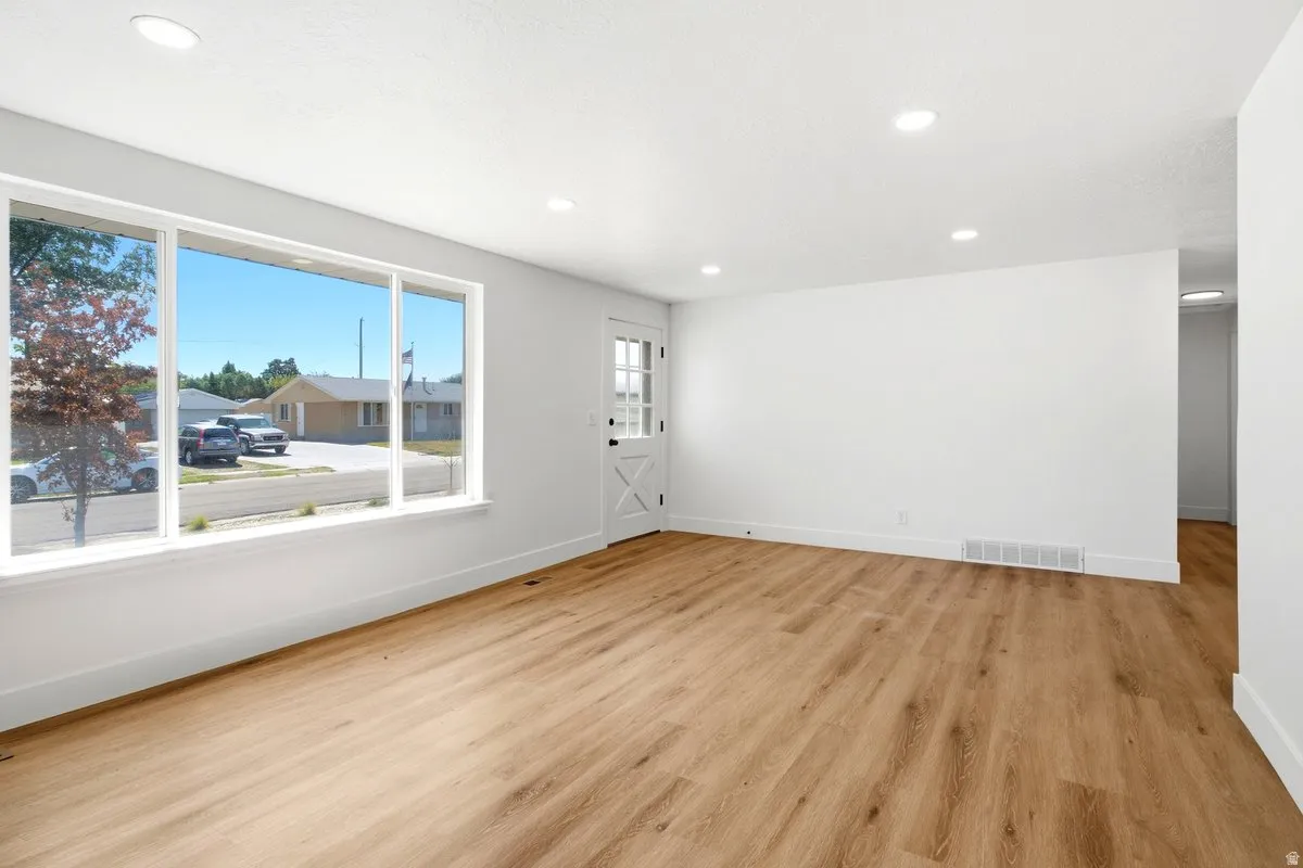 Spacious room featuring wood-finish flooring, recessed lighting, a large picture window, and a paneled entry door