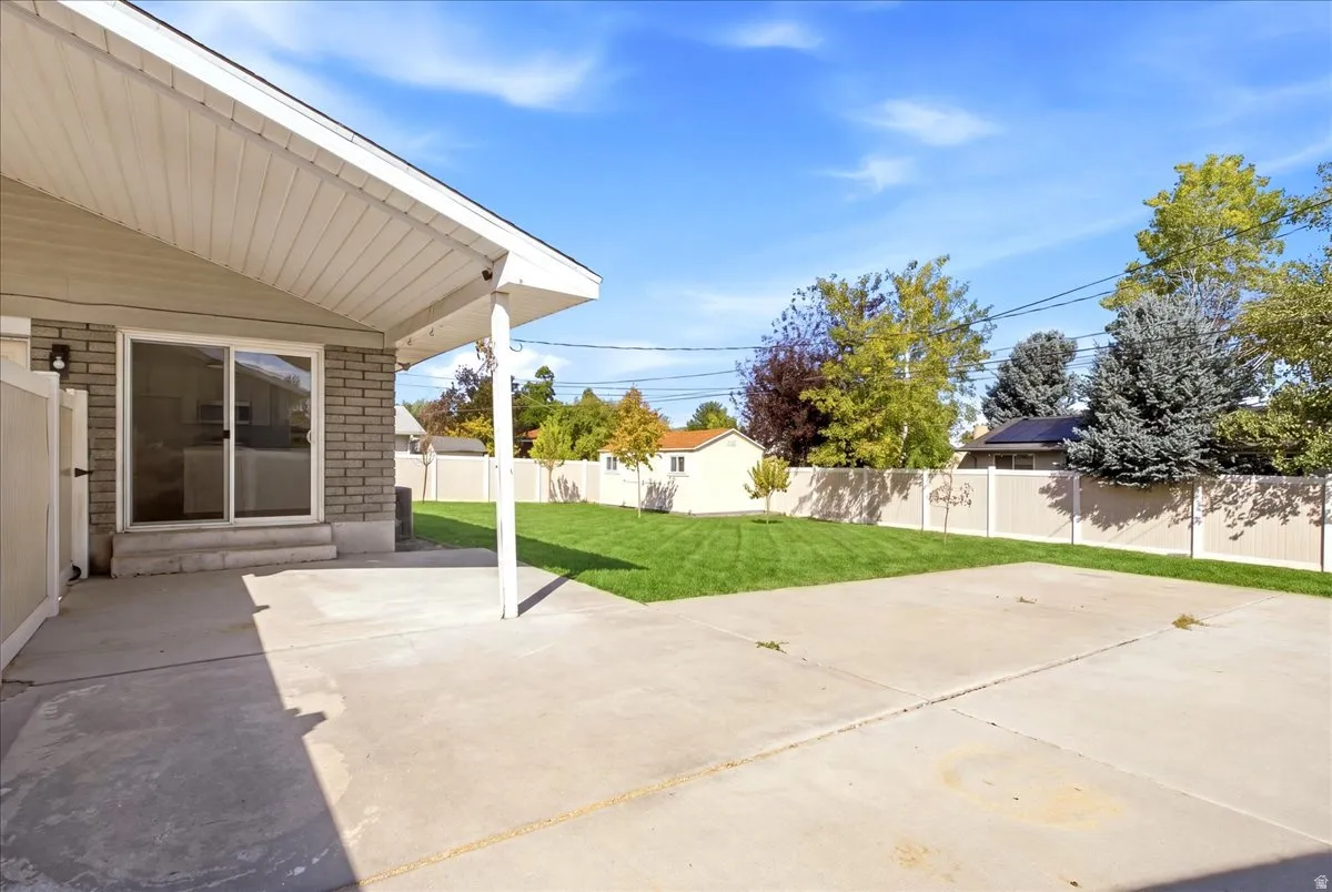 Expansive concrete patio with covered area, sliding glass door access, and a manicured lawn