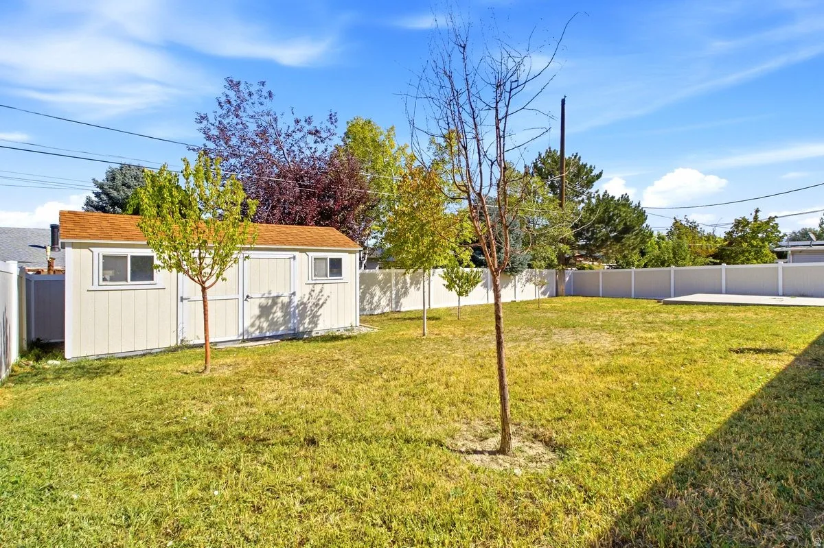 Expansive backyard featuring a storage shed with a shingled roof, a concrete patio, mature trees, and privacy fencing