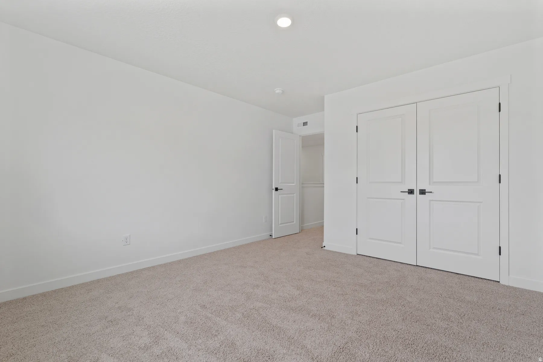 Plush carpeting throughout, bright white walls, recessed ceiling lighting, and a double-door closet with dark hardware
