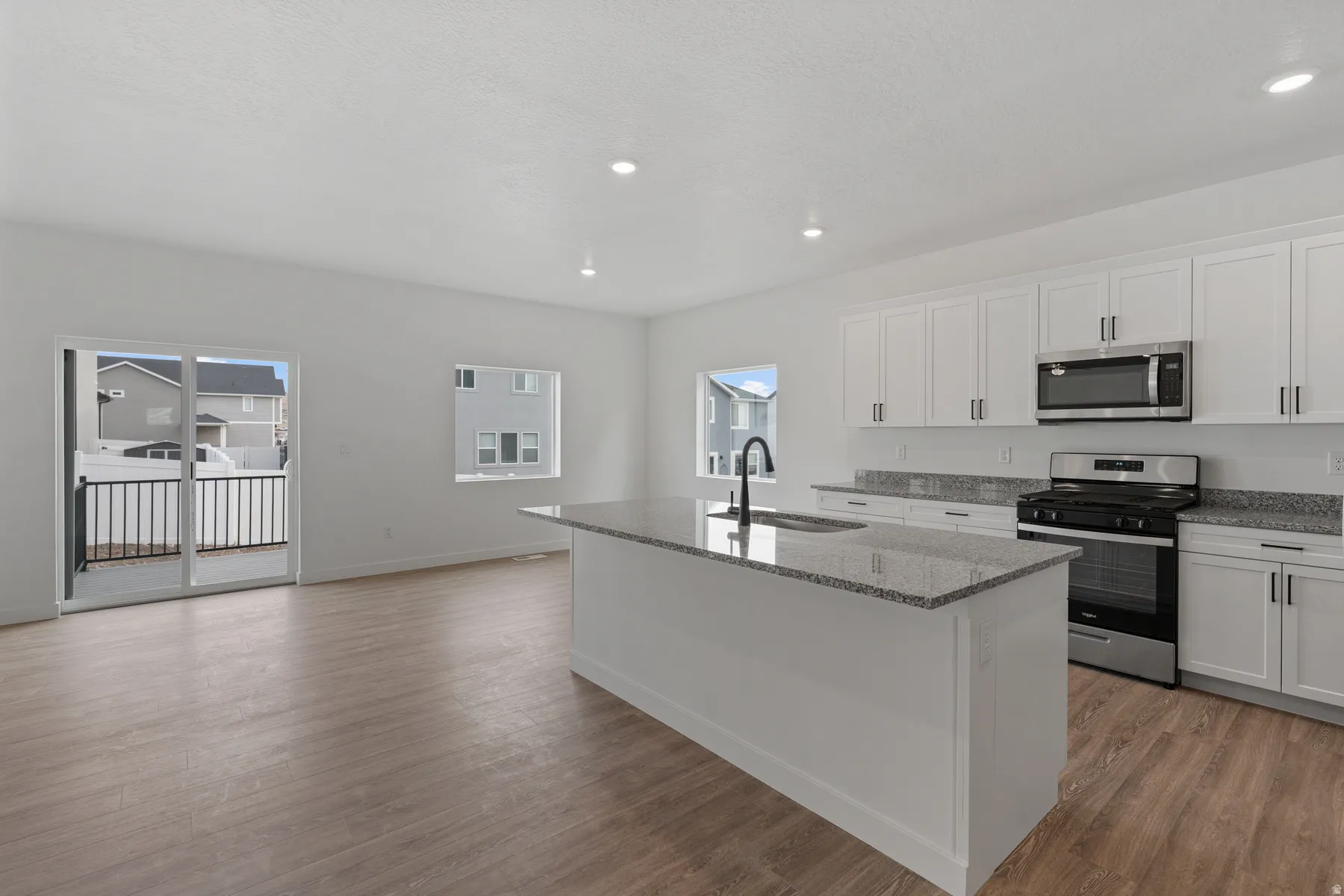 Kitchen featuring white cabinetry, a central island with an undermount sink, stone countertops, and stainless steel appliances