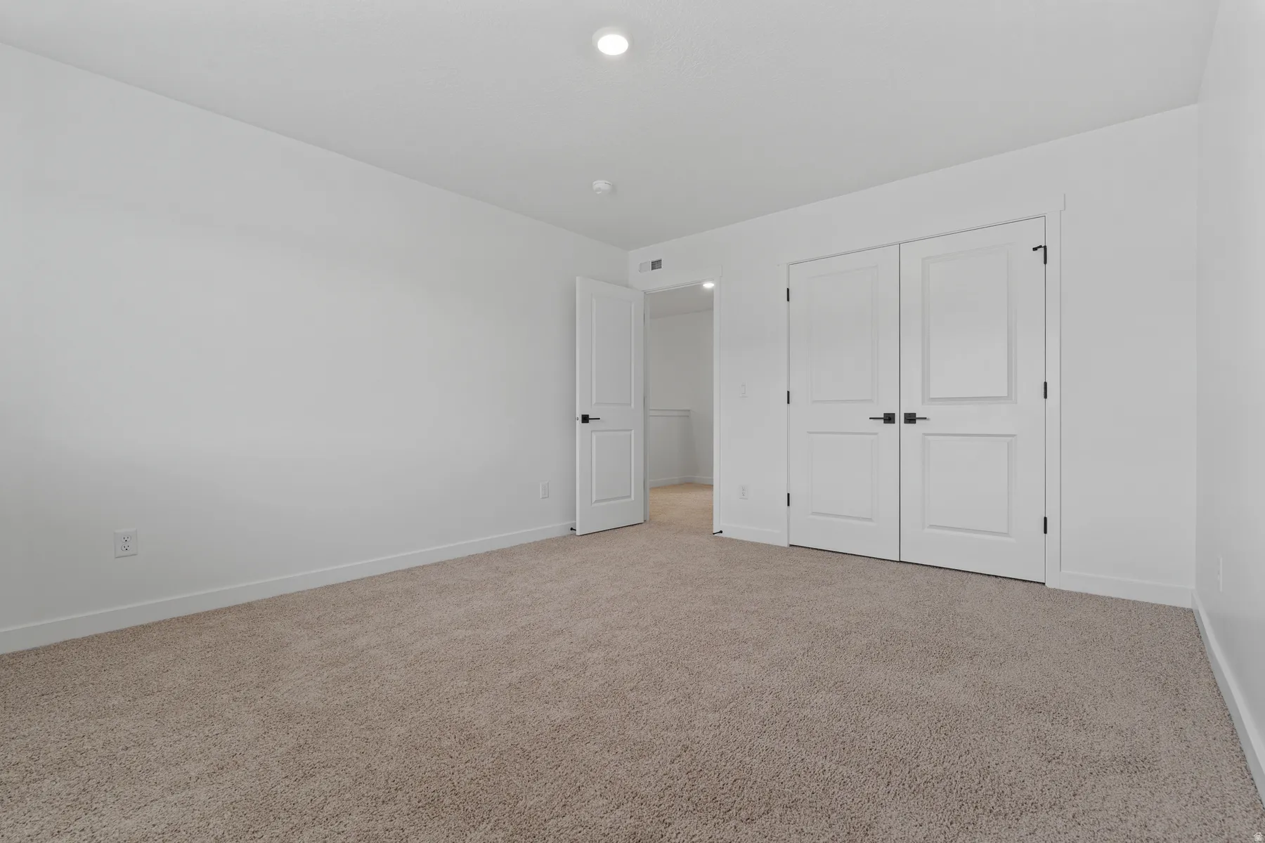 Recessed lighting illuminates the room, featuring plush carpeting and white walls