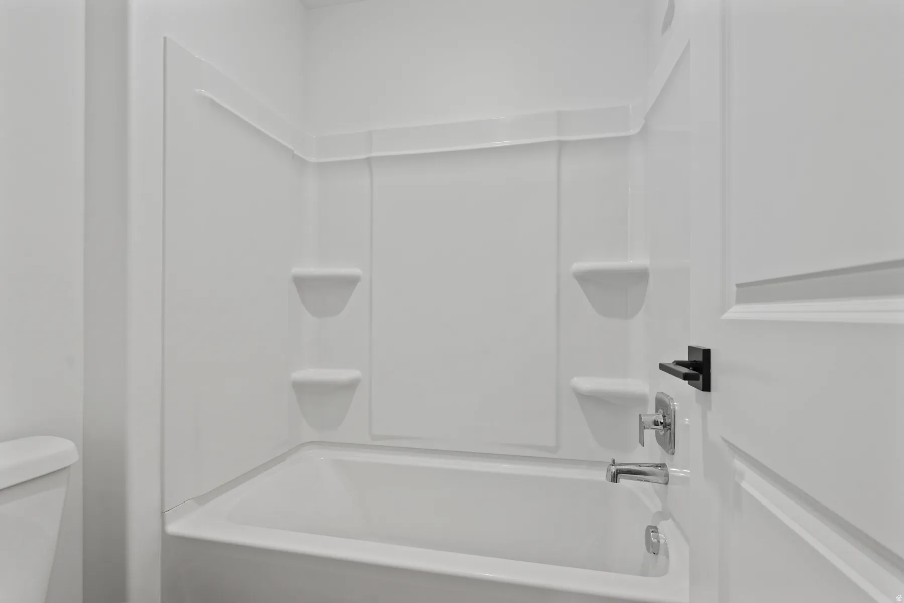 White tub and shower combination with integrated shelving, polished chrome fixtures, and a coordinating door with matte black hardware