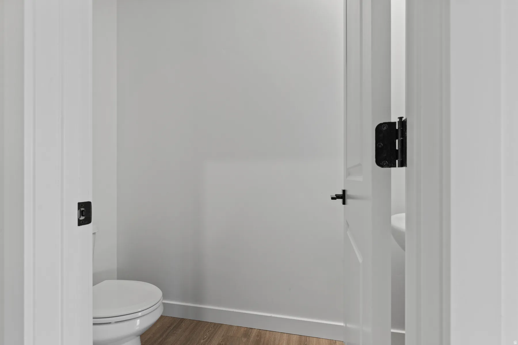 Wood-finish flooring with white trim, white walls, and a white interior door with black hardware