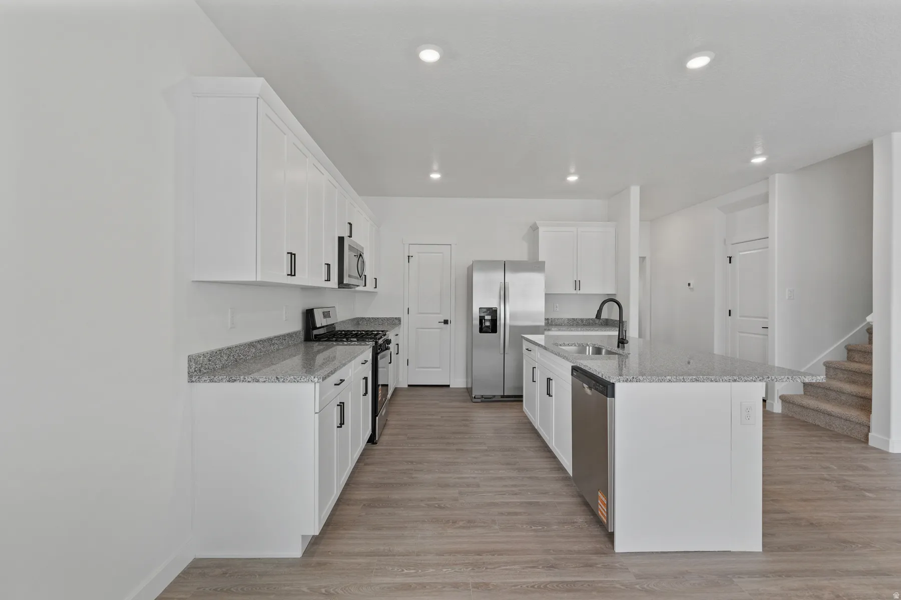 Modern kitchen featuring white cabinetry, stainless steel appliances, granite countertops, an island with a sink, and wood-finish flooring