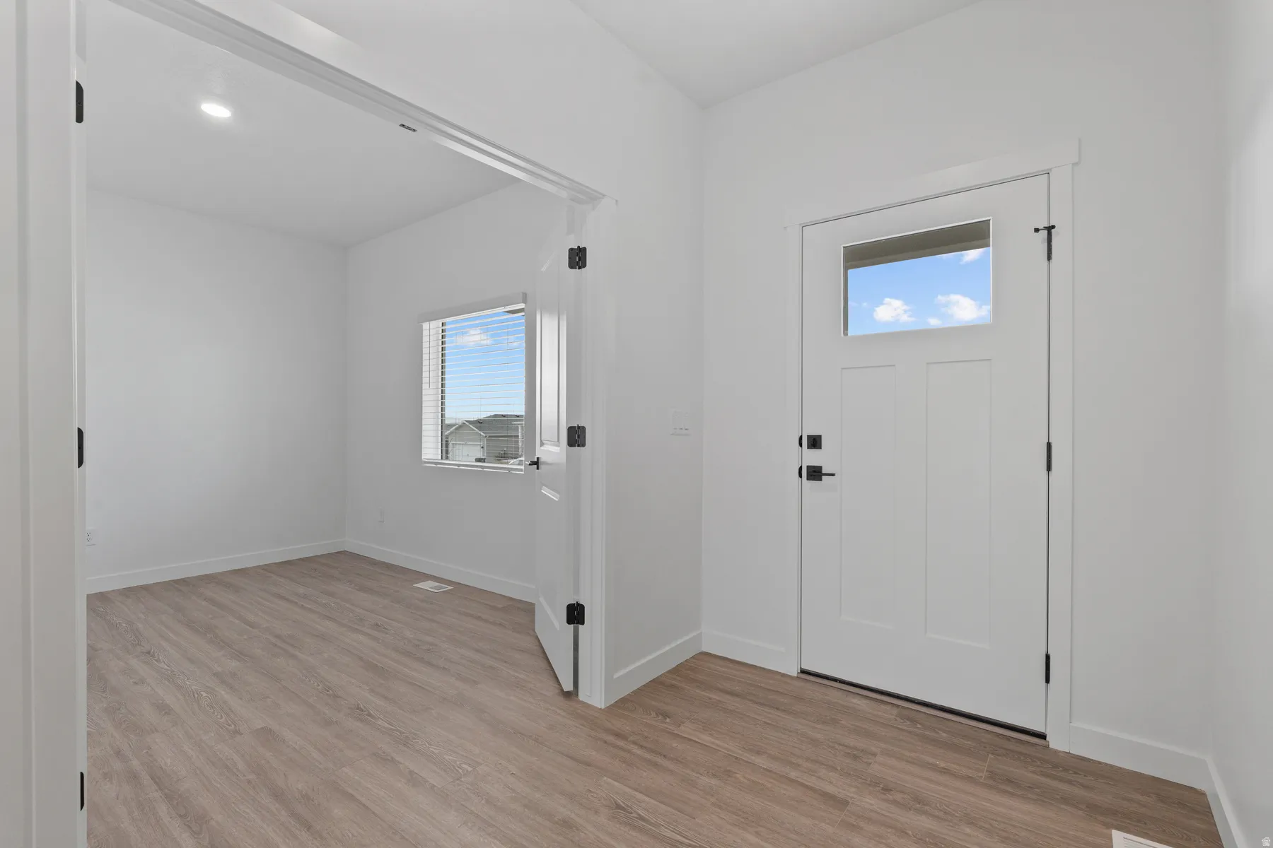 Entryway featuring wood-finish flooring, a white front door with a transom window, and modern black hardware