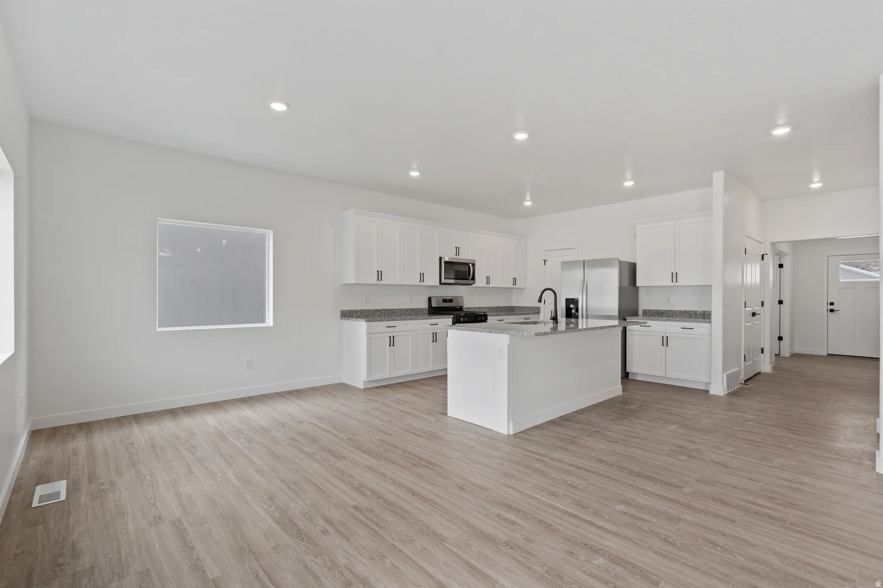 Open-concept living area featuring wood-finish flooring, recessed lighting, white cabinetry, a kitchen island with a sink, and stainless steel appliances