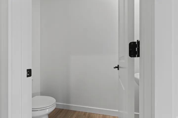 Wood-finish flooring with white trim, white walls, and a white interior door with black hardware