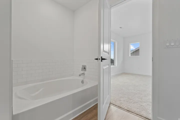 White subway tile surround with chrome fixtures, wood-finish flooring, white paneled door with matte black hardware, and two windows