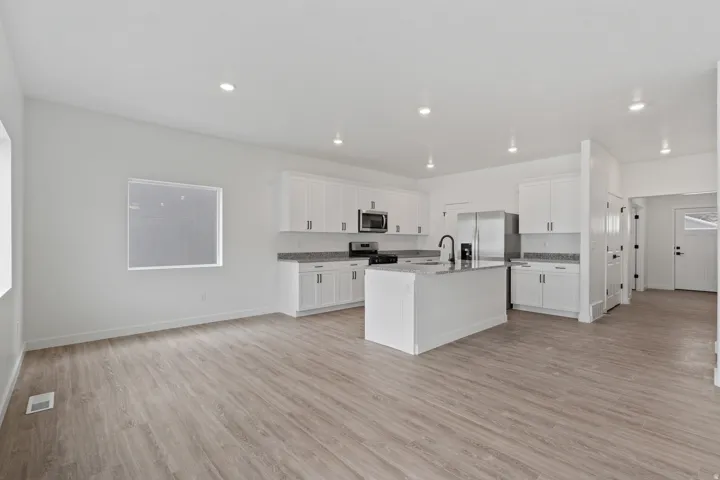 Open-concept living area featuring wood-finish flooring, recessed lighting, white cabinetry, a kitchen island with a sink, and stainless steel appliances