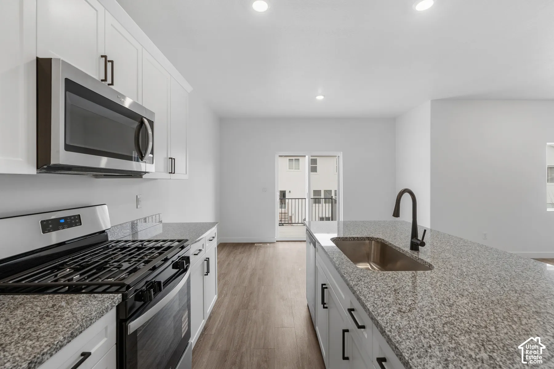 White cabinetry with matte black hardware, stainless steel appliances, granite countertops, and wood-finish flooring