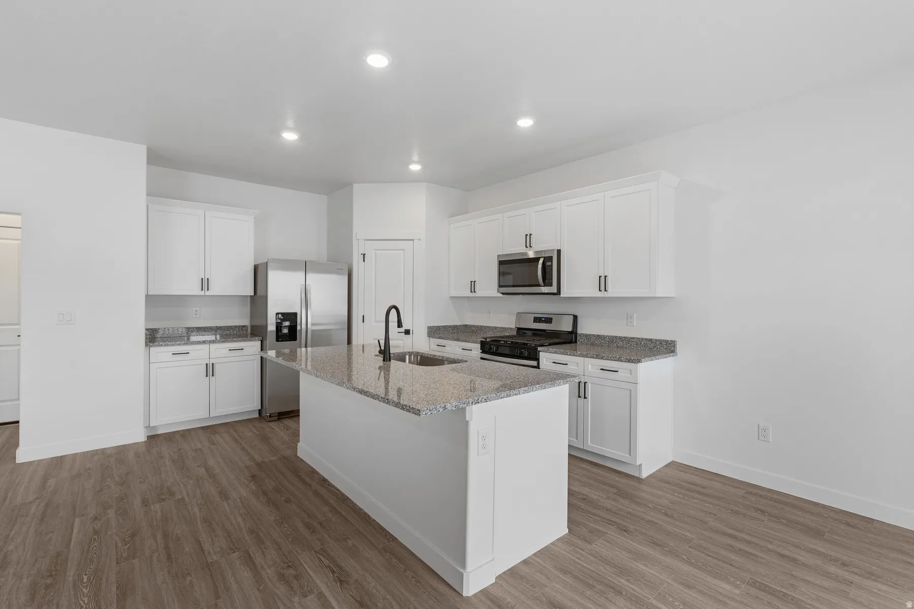 White cabinetry with matte black hardware, stainless steel appliances, granite countertops, and wood-finish flooring