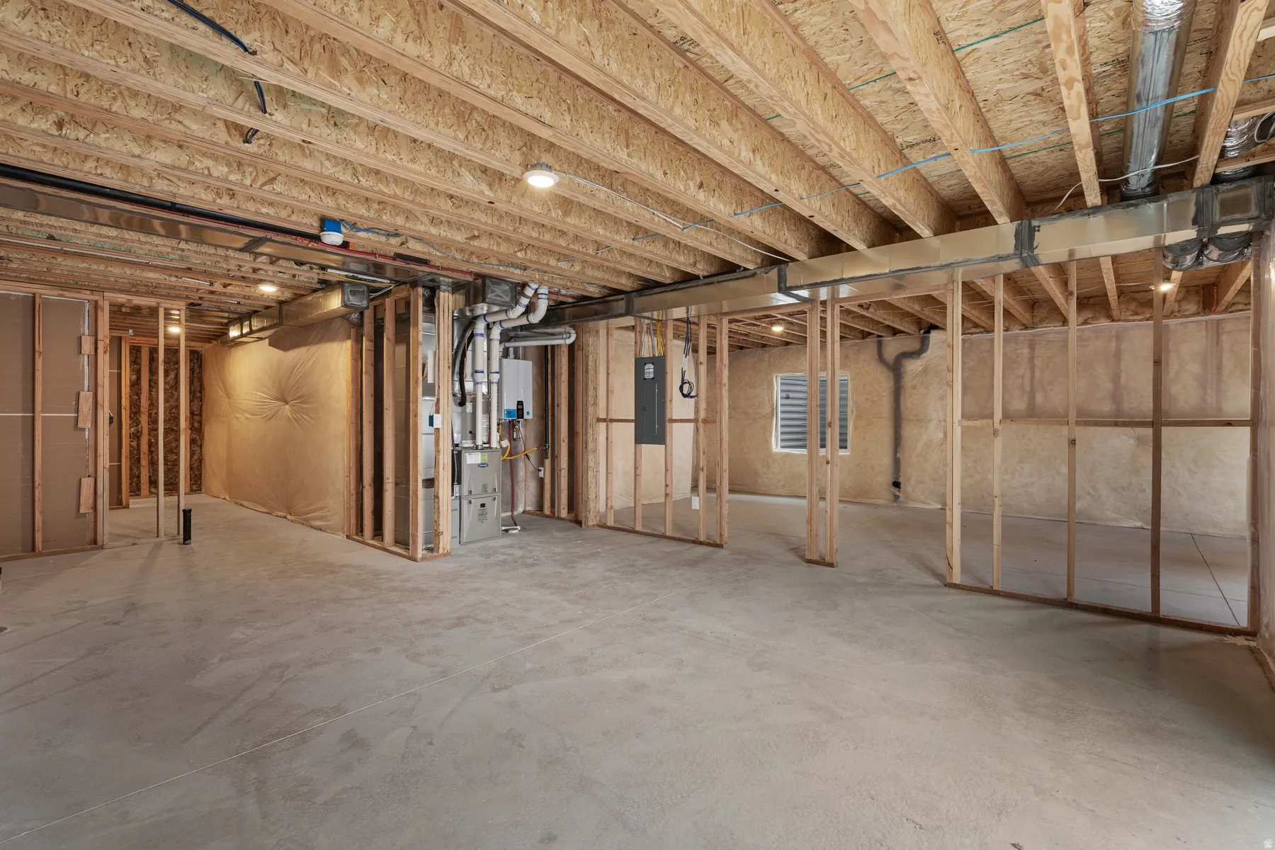 Unfinished basement with concrete flooring, exposed wood framing, and visible utility systems