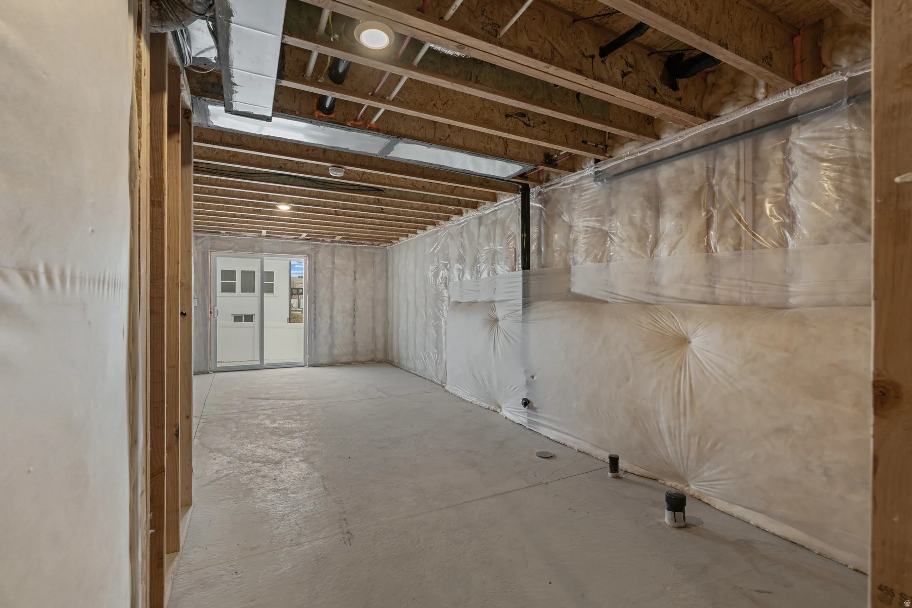 Unfinished lower level featuring exposed wood joists, concrete flooring, and an egress door