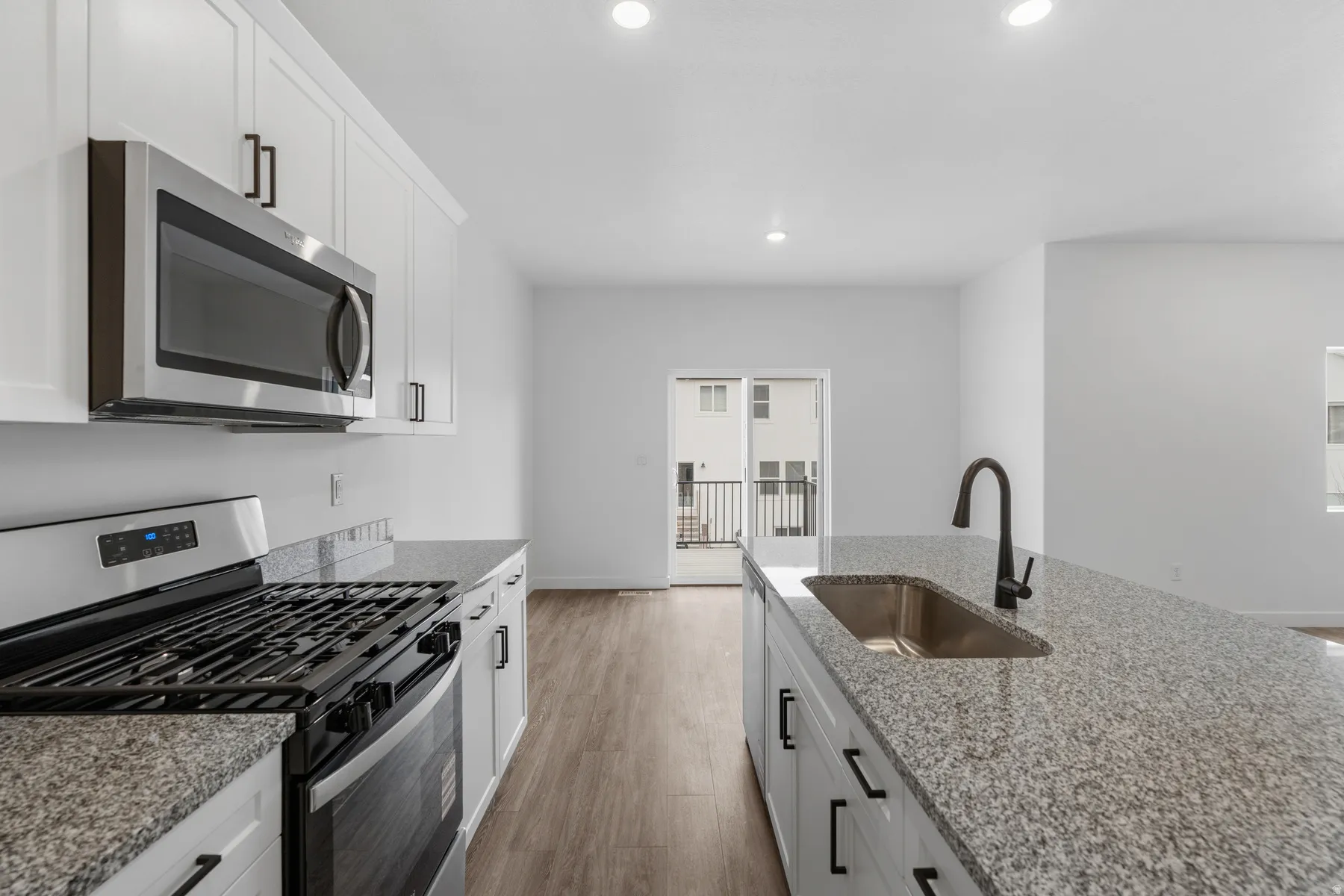 White cabinetry with matte black hardware, stainless steel appliances, granite countertops, and wood-finish flooring