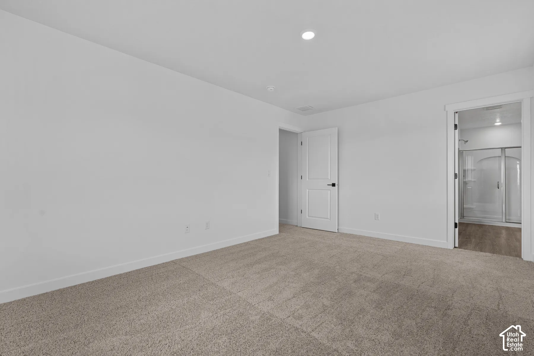 Recessed ceiling lighting, white walls, light-colored carpet, white interior door with black hardware, and a framed doorway