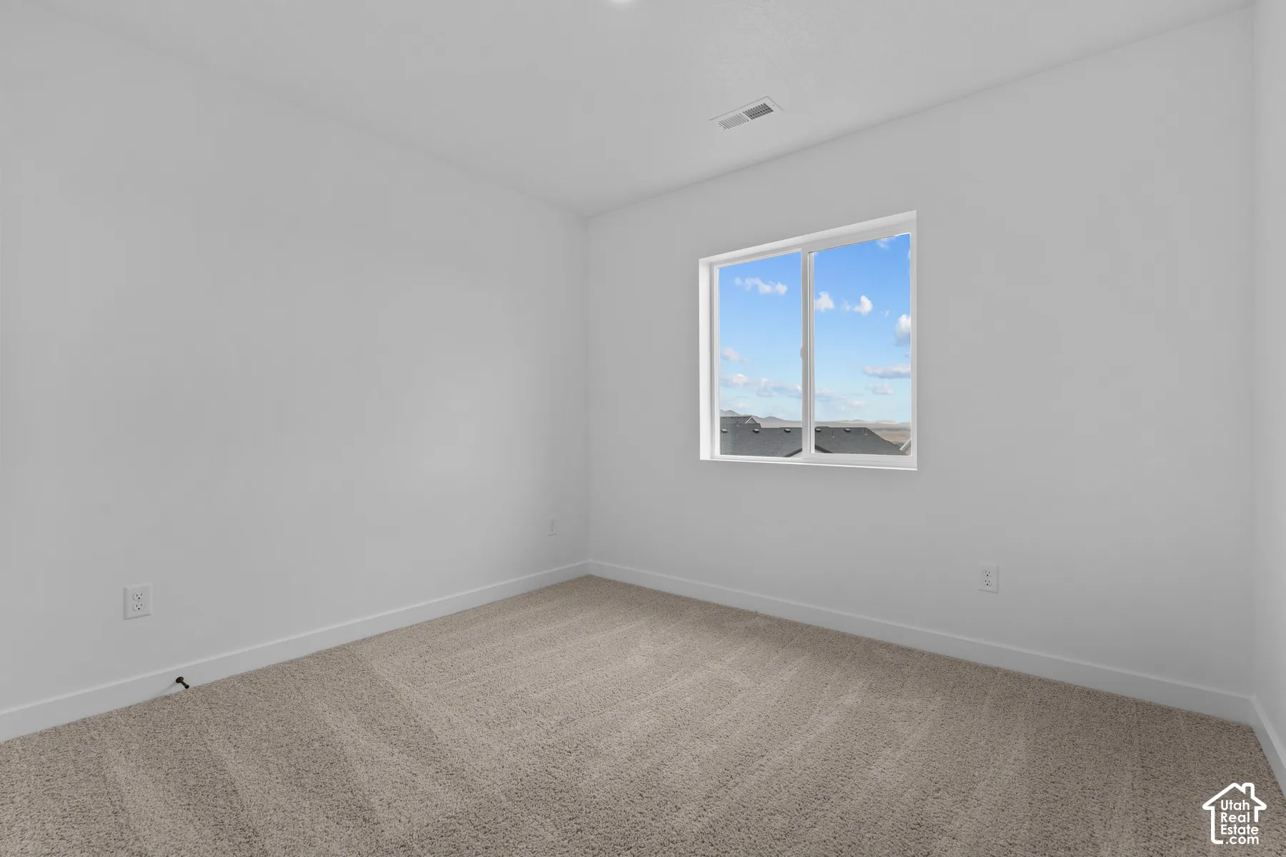 Neutral-toned carpeted flooring with a white trim, large window with white framing, and white painted walls