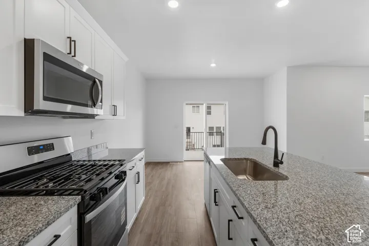 White cabinetry with matte black hardware, stainless steel appliances, granite countertops, and wood-finish flooring
