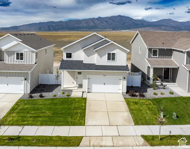 Contemporary stucco exterior with an attached garage, landscaped front yard with a lawn, concrete driveway, and a mountain backdrop