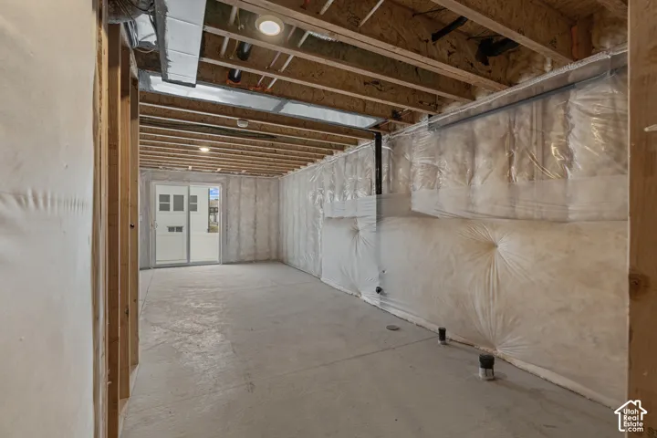Unfinished lower level featuring exposed wood joists, concrete flooring, and an egress door