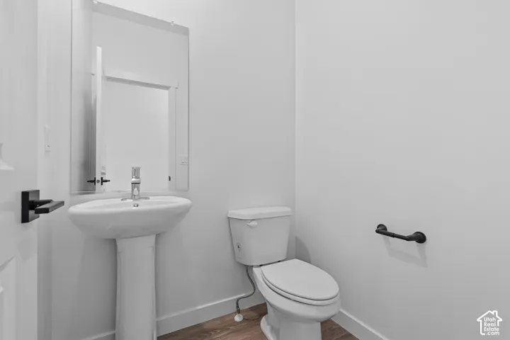 Pedestal sink with chrome faucet, wall-mounted mirror, white toilet, matte black door hardware, and wood-finish flooring