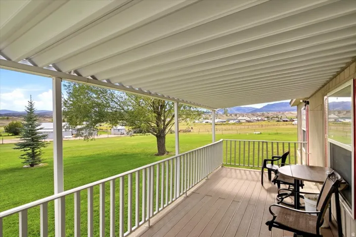 Covered porch with wood-finish decking, white railings, and direct access to a grassy expanse