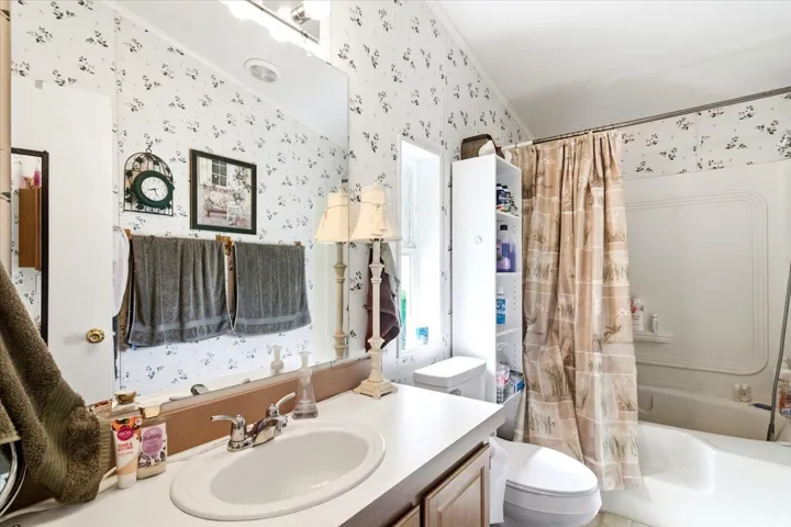 Bathroom featuring a vanity with an integrated sink, wall-mounted mirror, wood-finish cabinetry, a full-size bathtub with shower, and a built-in storage tower