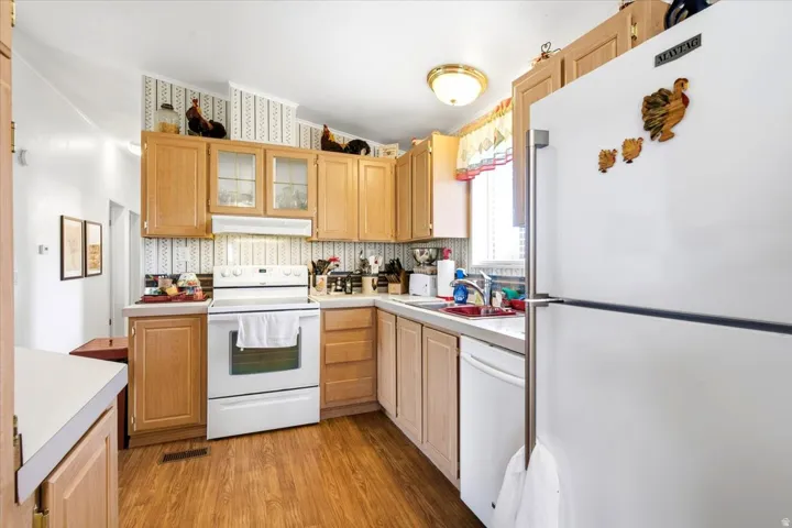 Laminate flooring, wood-finish cabinetry, white appliances, and a double basin sink