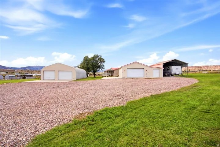 Gravel driveway leading to multiple outbuildings, including a Quonset hut-style structure with two garage doors, an additional garage building with a single door, and a covered carport