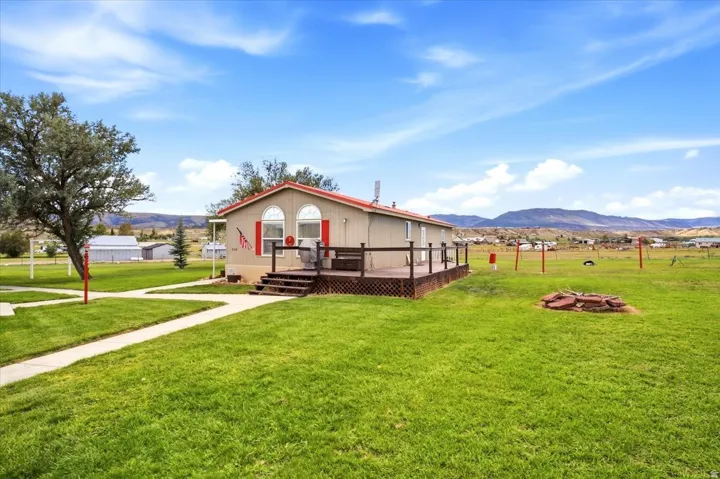 Expansive green lawn with a defined concrete pathway, leading to a home featuring a red roof and a spacious wooden deck with railings