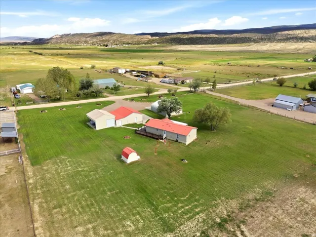 Expansive property featuring multiple structures, mature trees, open green spaces, and mountain terrain backdrop