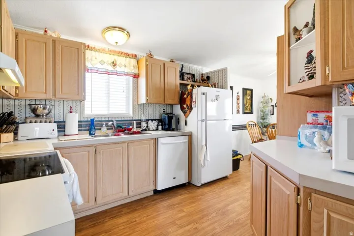 Kitchen featuring light wood-finish cabinetry, light countertops, wood-finish flooring, a built-in dishwasher, and a window with blinds