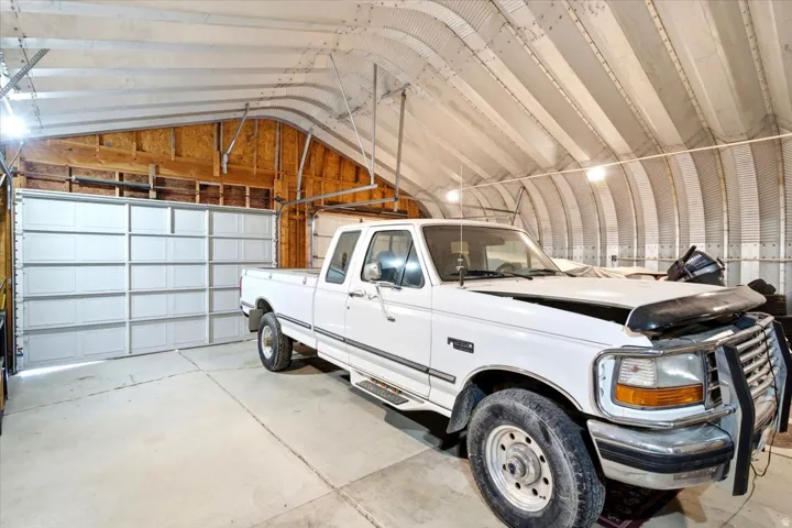 Quonset hut-style structure featuring a concrete floor, exposed wood framing, and multiple overhead light fixtures