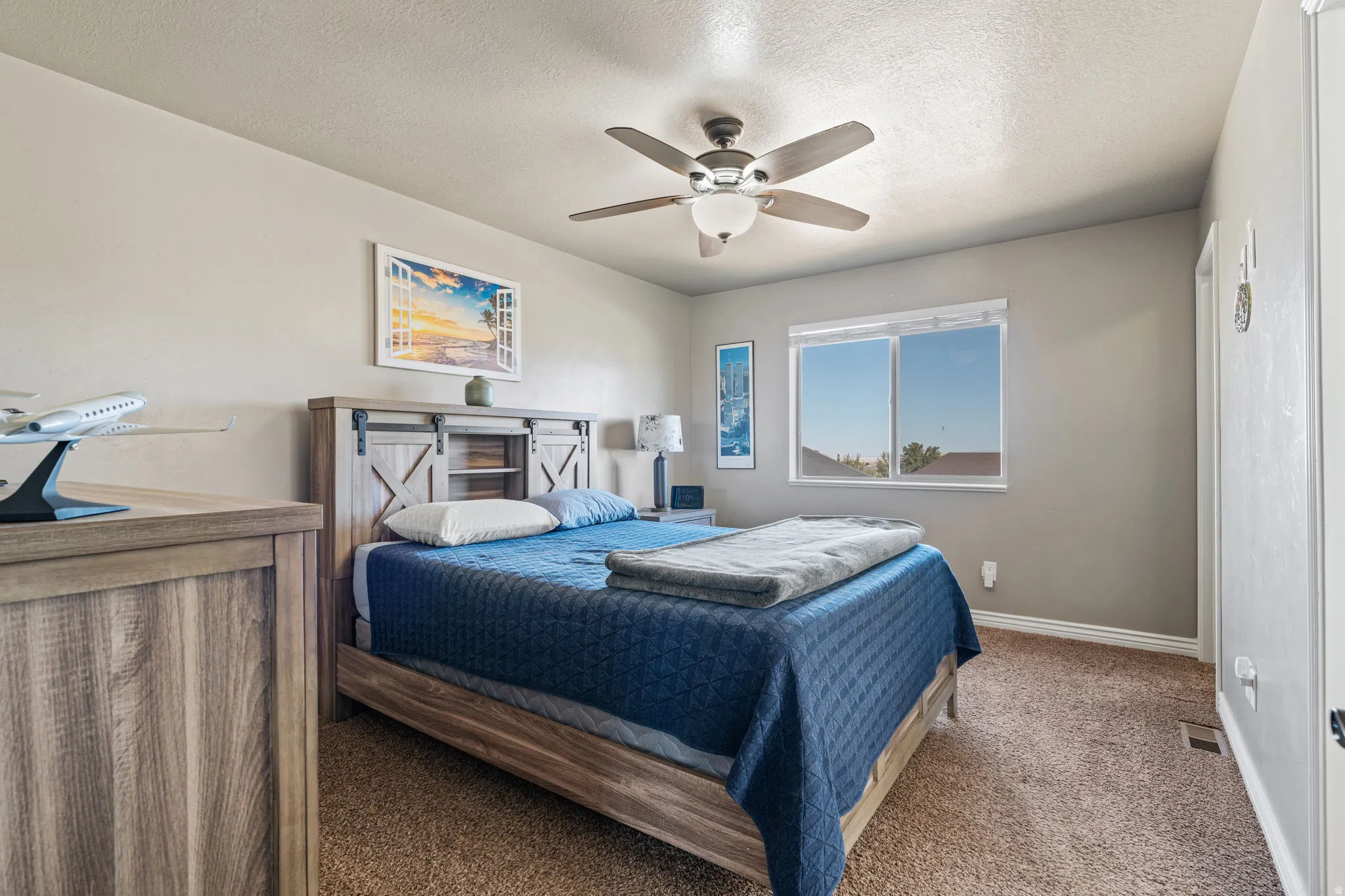 Ceiling fan with integrated lighting, window with white trim, light neutral wall paint, and textured carpet flooring