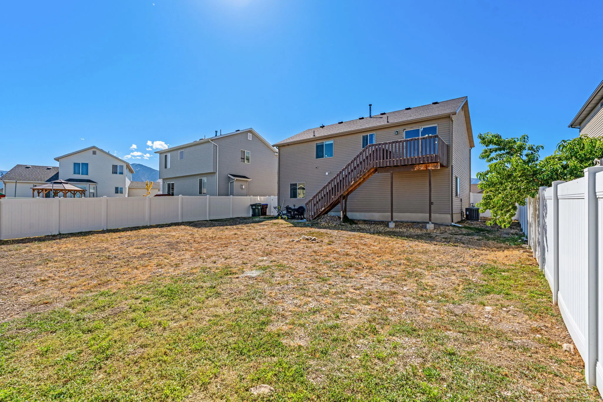 Expansive backyard featuring a privacy fence, wood deck, and exterior stairs