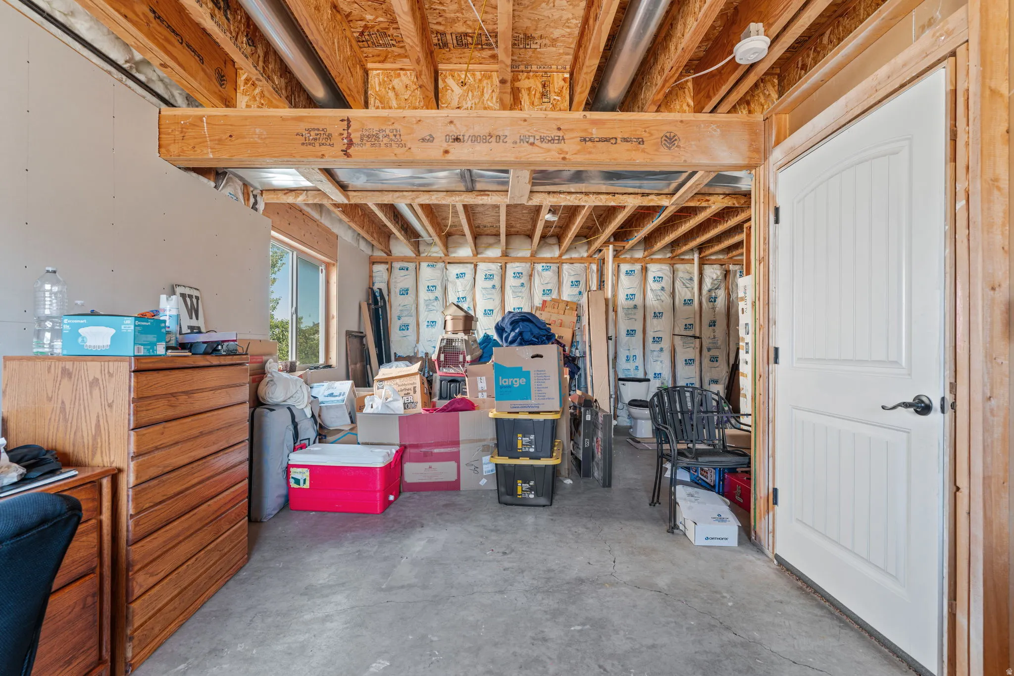 Unfinished basement space featuring exposed wood joists, a window, and a white paneled door
