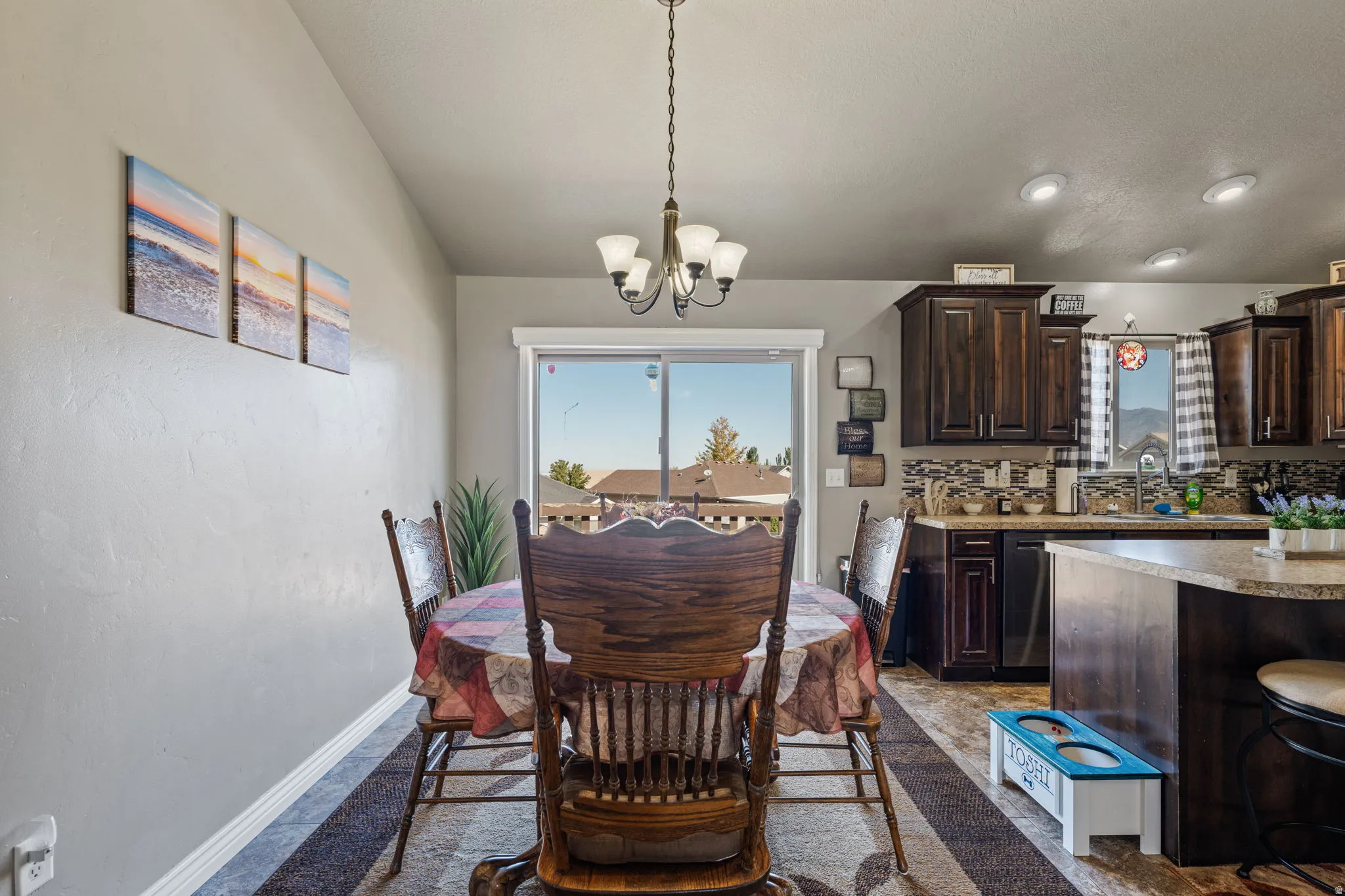 Sliding glass door, recessed ceiling lighting, pendant light fixture, dark wood-finish cabinetry, tile backsplash