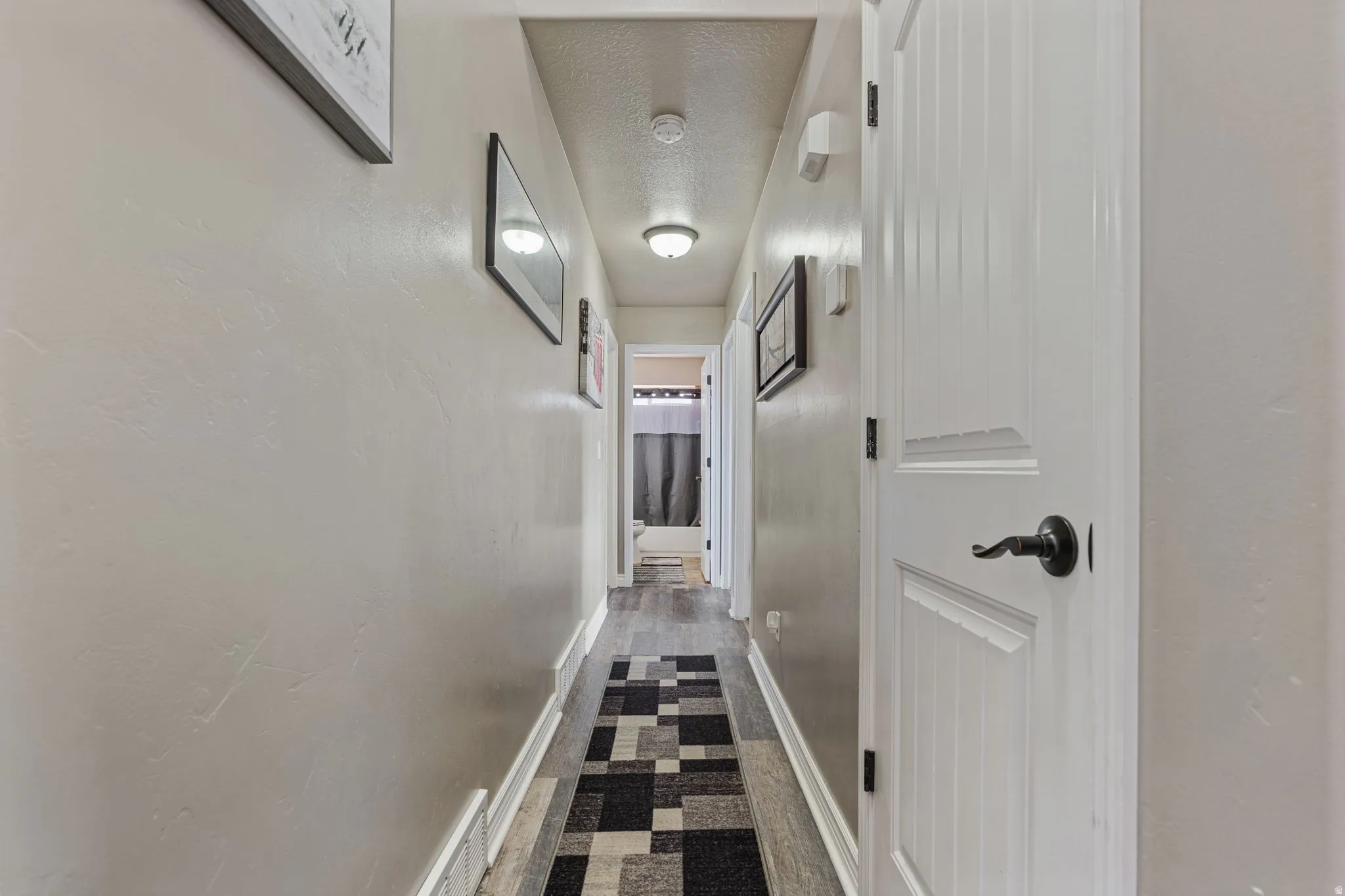 Hallway featuring wood-finish flooring, recessed lighting, and a paneled door with matte black hardware