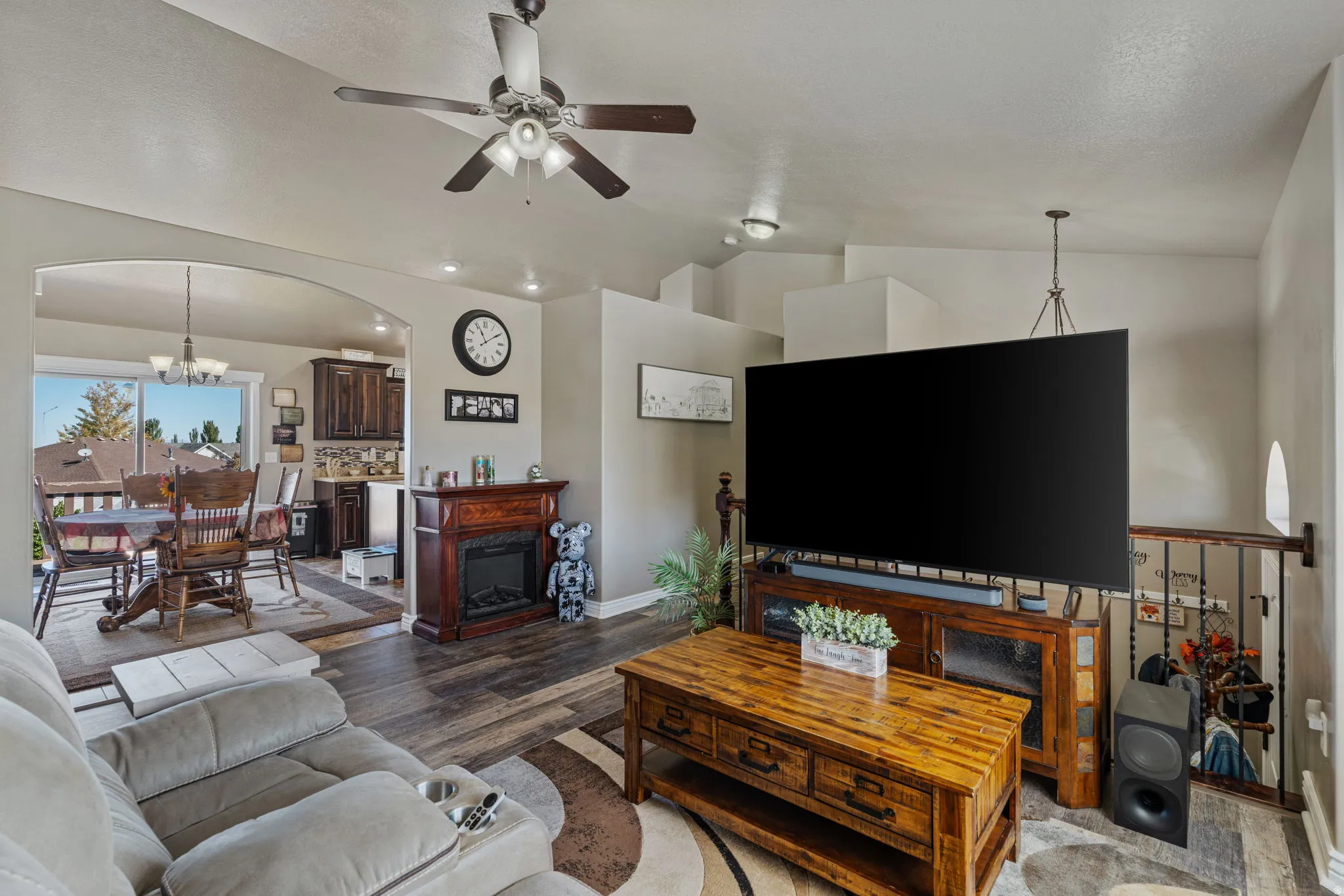 Arched entryway to the dining area, wood-finish flooring, ceiling fan, decorative fireplace, and wrought iron railing