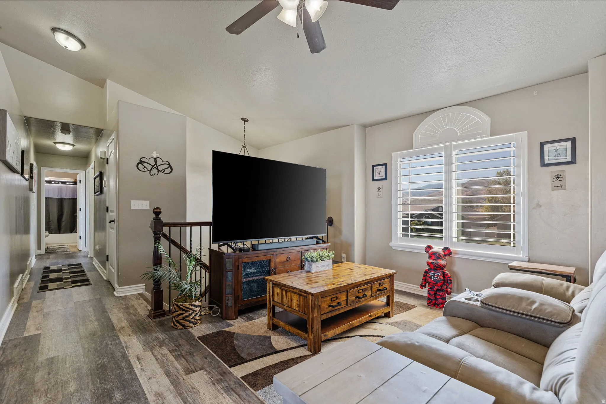 Vaulted ceilings with a ceiling fan, wood-finish flooring, white window shutters, and a banister with dark wood railing