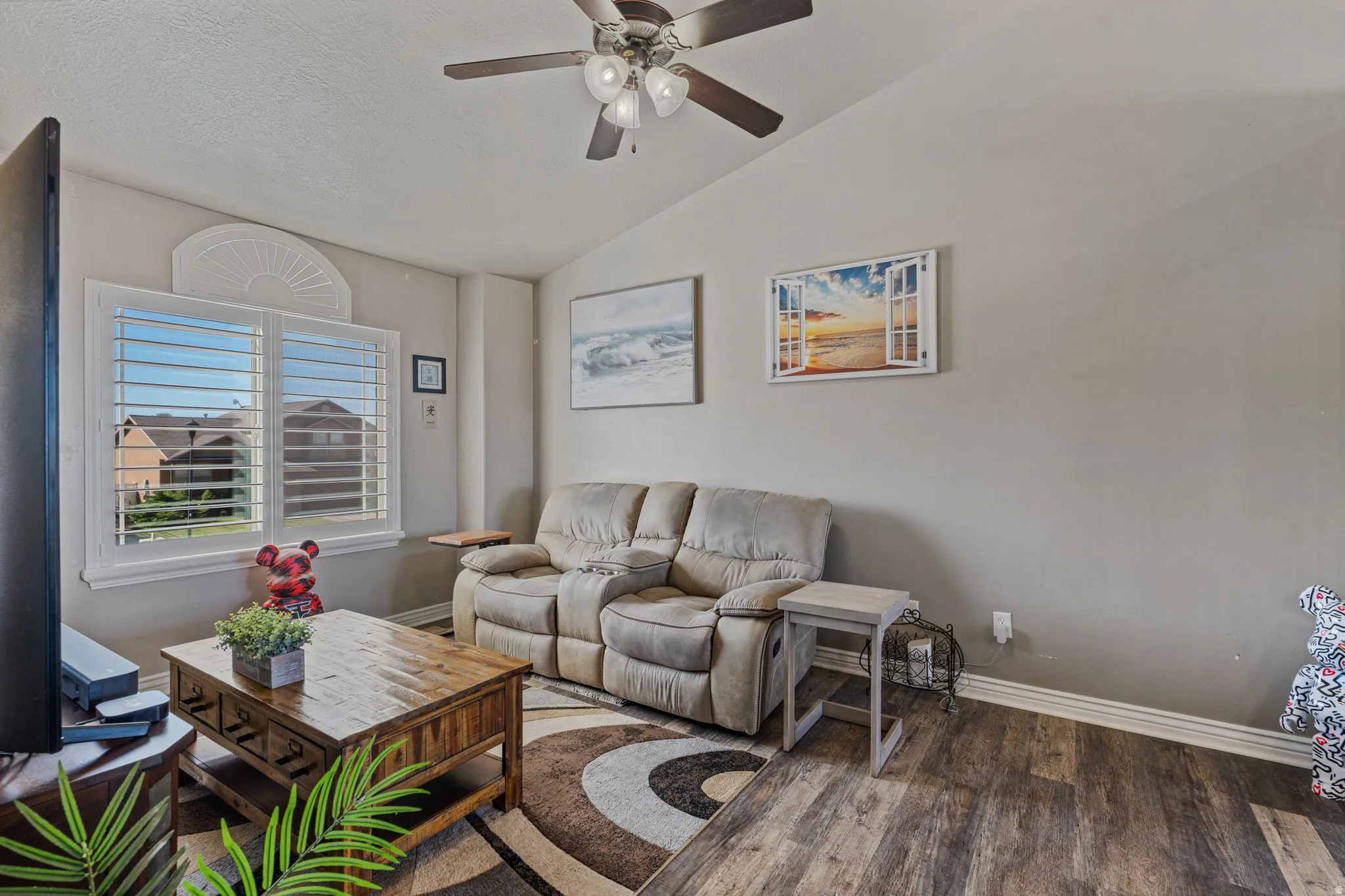 Vaulted ceiling with a ceiling fan, window with plantation shutters, wood-finish flooring, and neutral wall tones