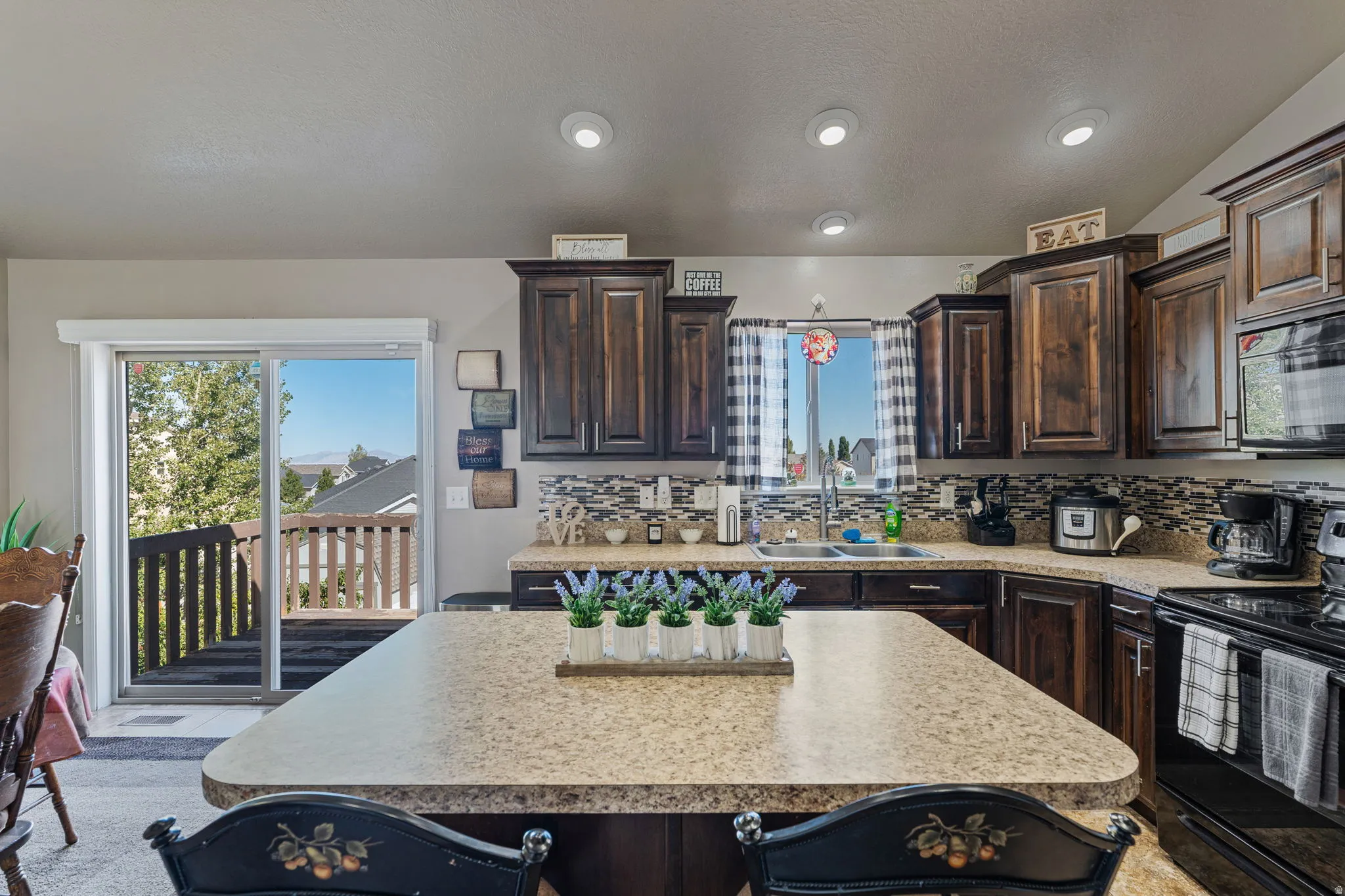 Kitchen featuring dark wood-finish cabinetry, a patterned tile backsplash, a kitchen island with a light-toned countertop, and recessed lighting