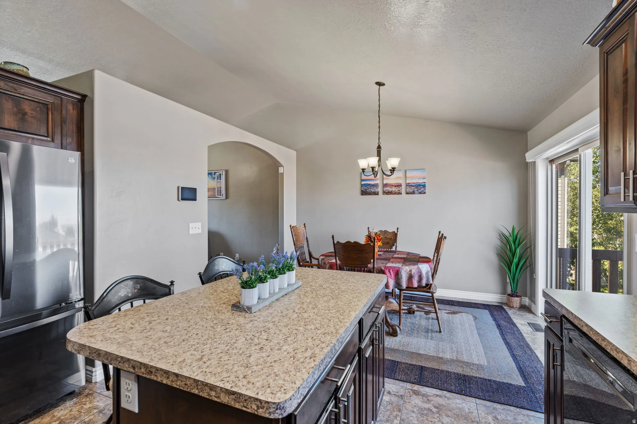 Kitchen island with composite countertop, dark wood-finish cabinetry, stainless steel refrigerator, and recessed lighting