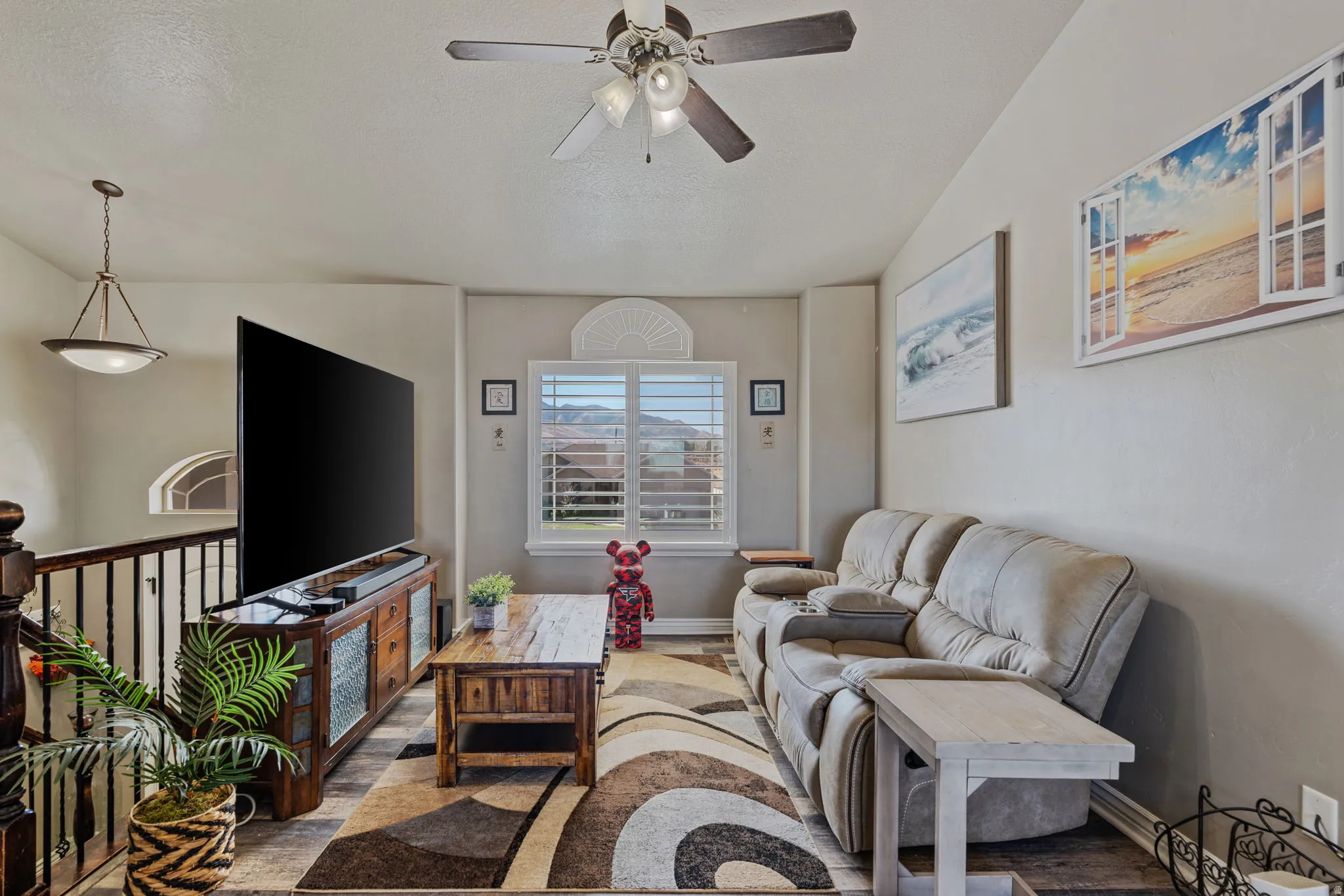 Vaulted ceiling with a ceiling fan light fixture, wood-finish flooring, and a window with plantation shutters