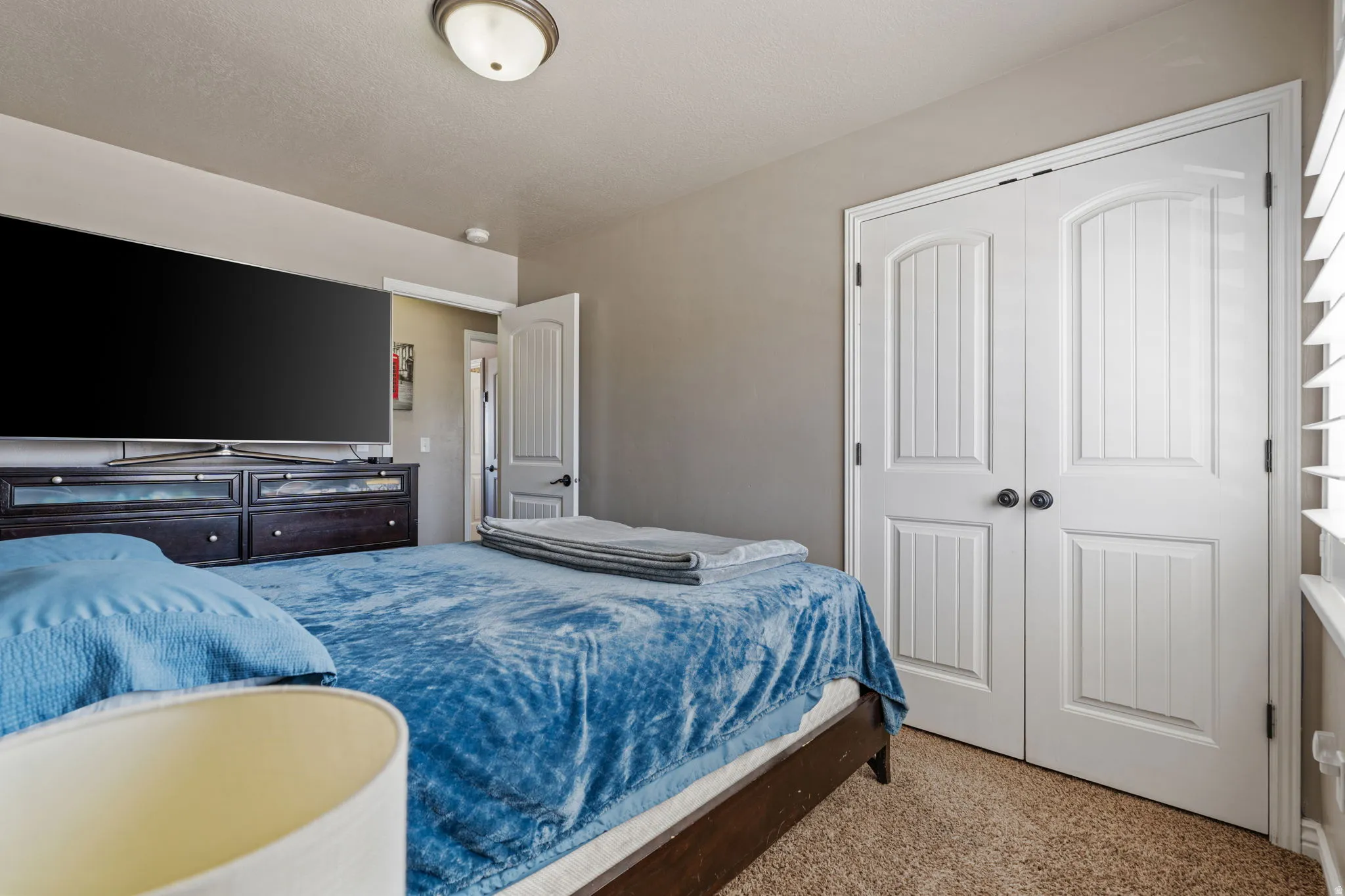 Recessed lighting, neutral wall tones, textured carpeting, white plantation shutters, and white paneled bi-fold doors